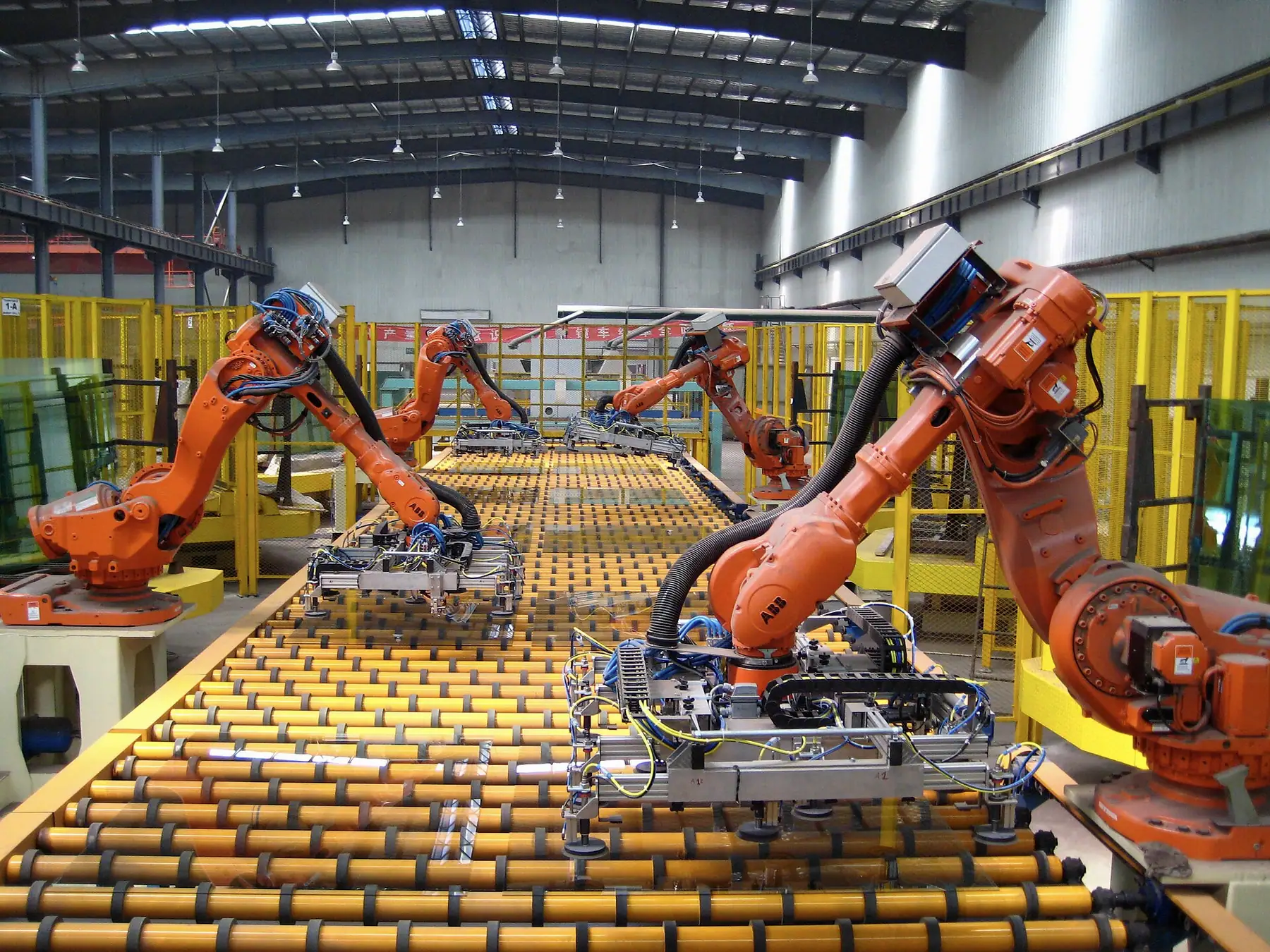 Makaralı transfer hattı boyunca vakum tutuculu turuncu robotların levha taşıdığı hat
