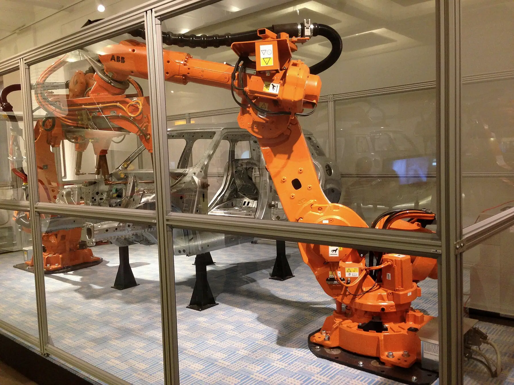 Koruma bölmesi içinde gövde parçası üzerinde çalışan turuncu robotlar