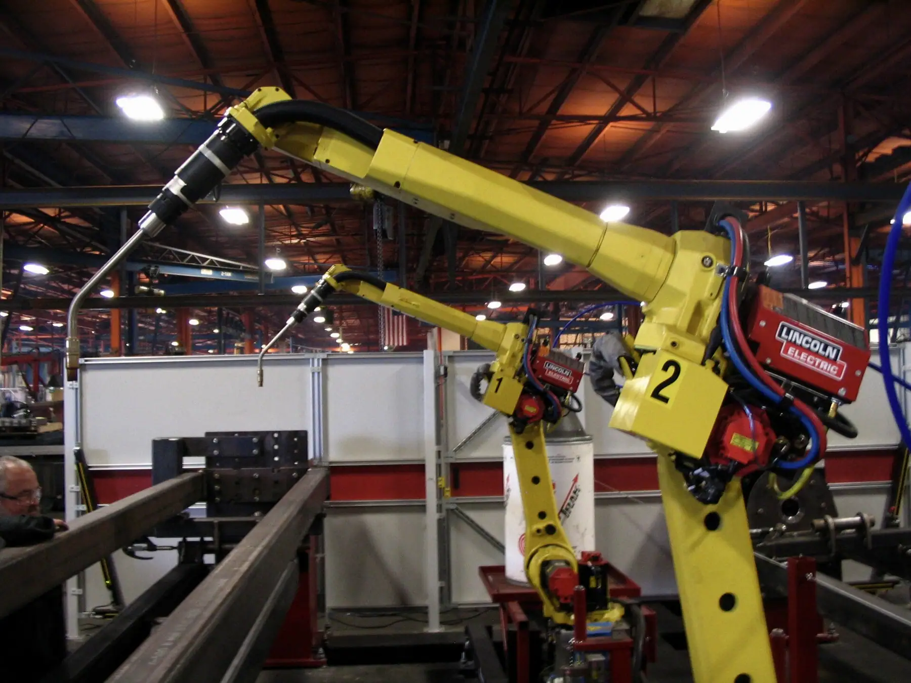 Kaynak hattının üzerinde konumlanmış sarı robot kolları ve fabrika tavanı