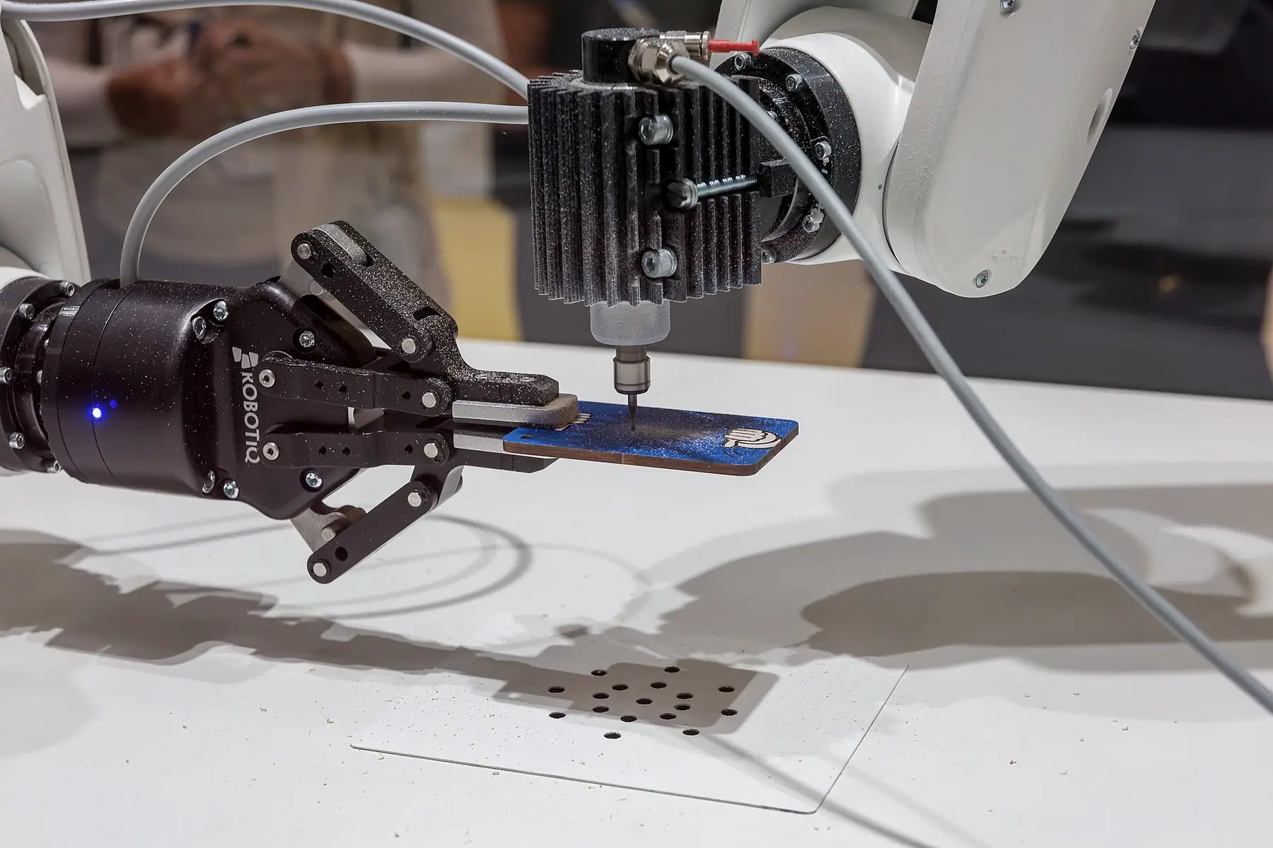 Robot bileğinde üç parmaklı elektrikli tutucu ve vidalama ünitesinin bir kartı konumladığı yakın plan