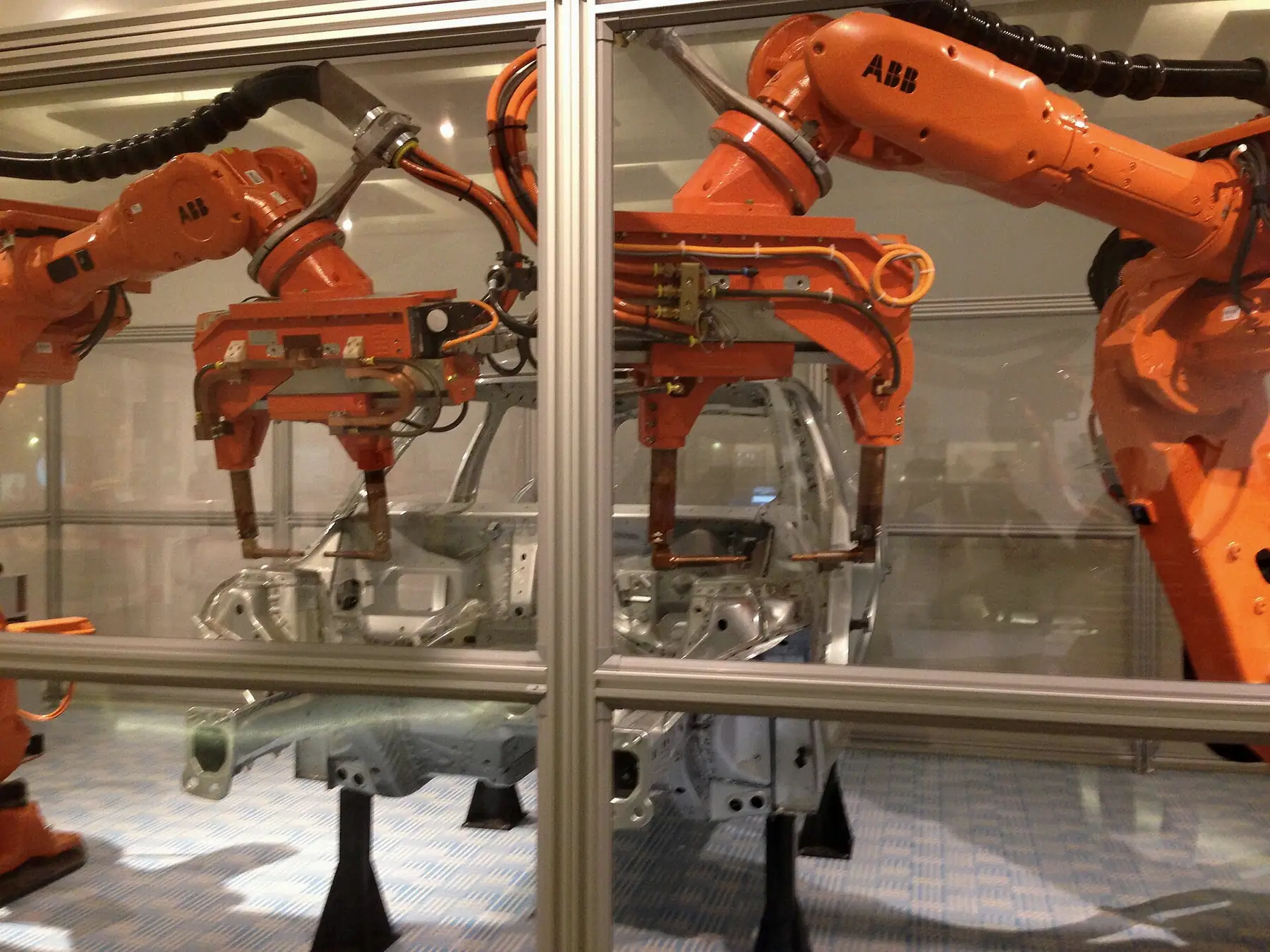 Cam bölmeli hücrede gövde parçası üzerinde çalışan turuncu kaynak robotları