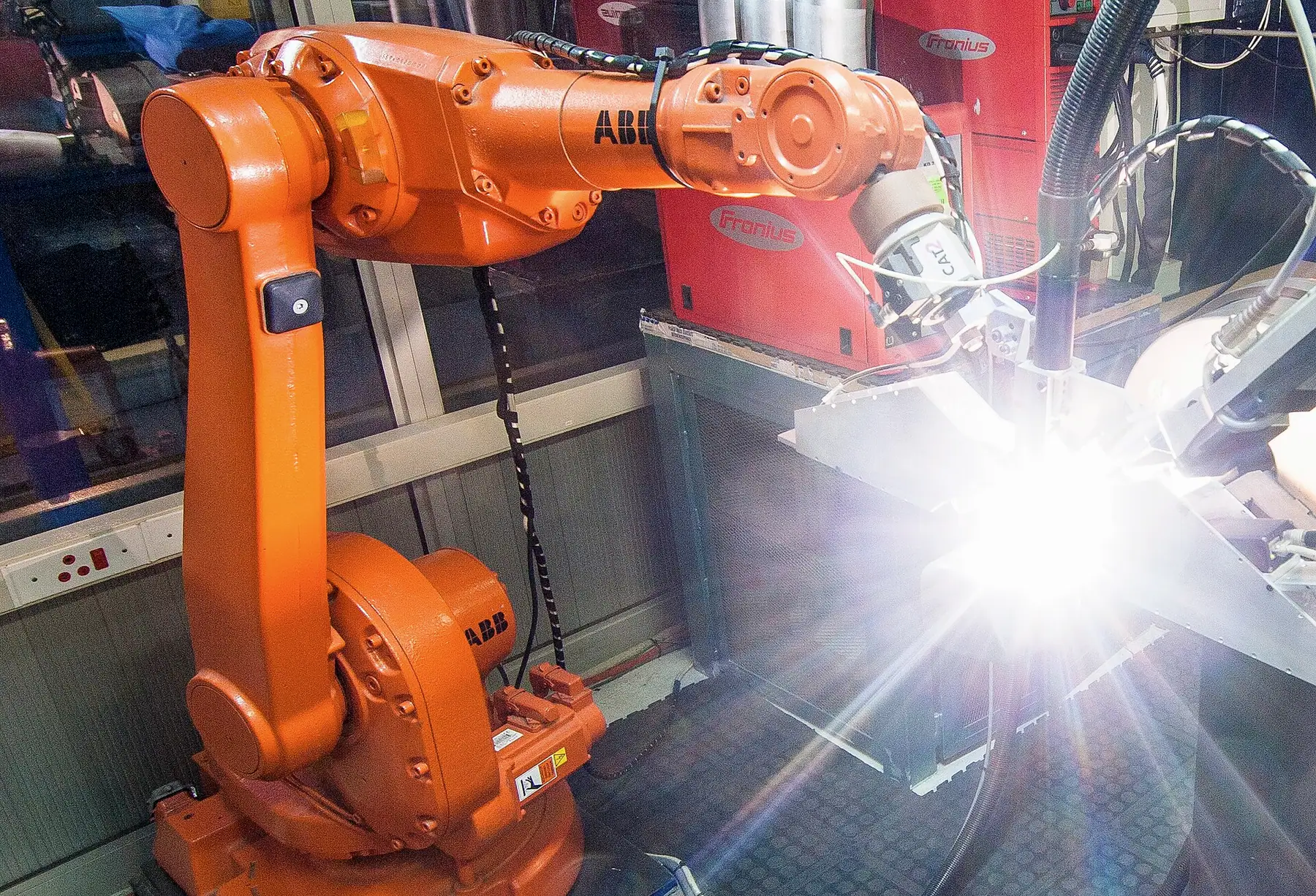 Turuncu kaynak robotunun alüminyum parça üzerinde parlak ark oluşturduğu an