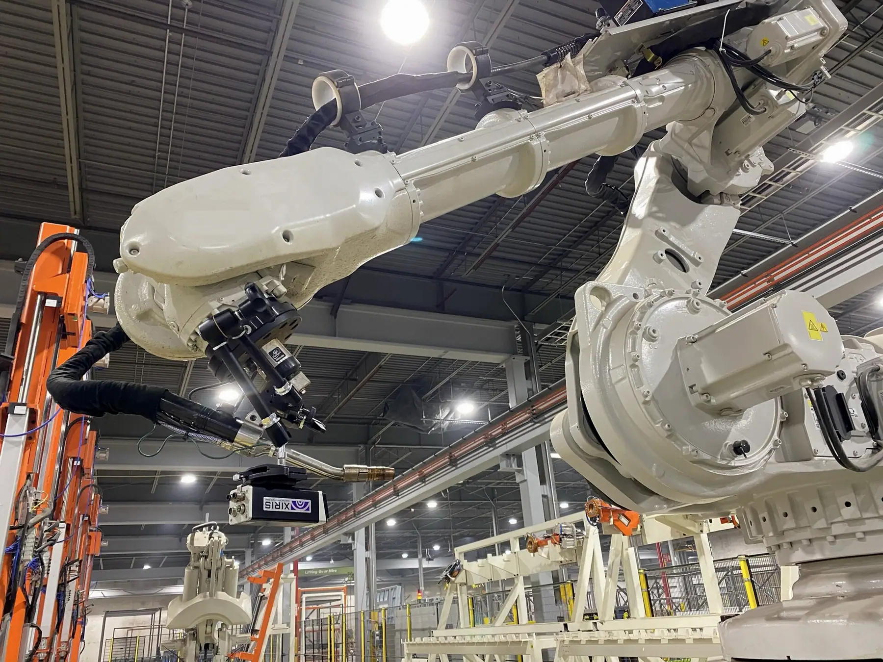 Kaynak izleme kamerasıyla donatılmış iki beyaz robotlu kaynak düzeni